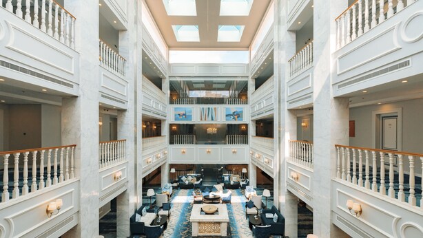 A spacious atrium with a high ceiling, marble floors, and a central seating area with sofas and tables. - Julnar Hotel (Unaizah)