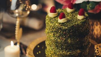 A cake on a golden stand with a candle and a glass of wine in the background.