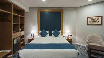 Habitación de hotel con una cama grande, dos mesitas de noche con lámparas, un armario, una silla y un cuadro en la pared.