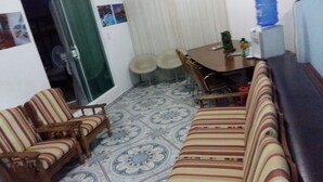 A small living area with a sofa, two armchairs, a dining table with four chairs, and a water dispenser. - Pousada Recanto Dom Lázaro (Cesario Lange)
