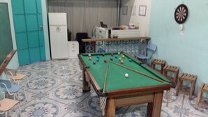 A pool table in a room with patterned floor tiles, a refrigerator, and a dartboard on the wall. - Pousada Recanto Dom Lázaro (Cesario Lange)