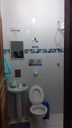 A small bathroom with a toilet, sink, and a mirror. There are signs on the wall, a hand dryer, and a shower area. - Pousada Recanto Dom Lázaro (Cesario Lange)