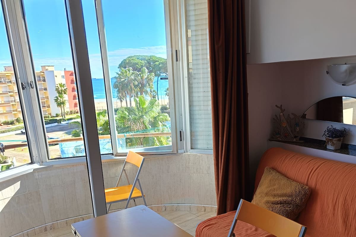 A balcony with a table and chairs, a sofa, and a view of the ocean and buildings.