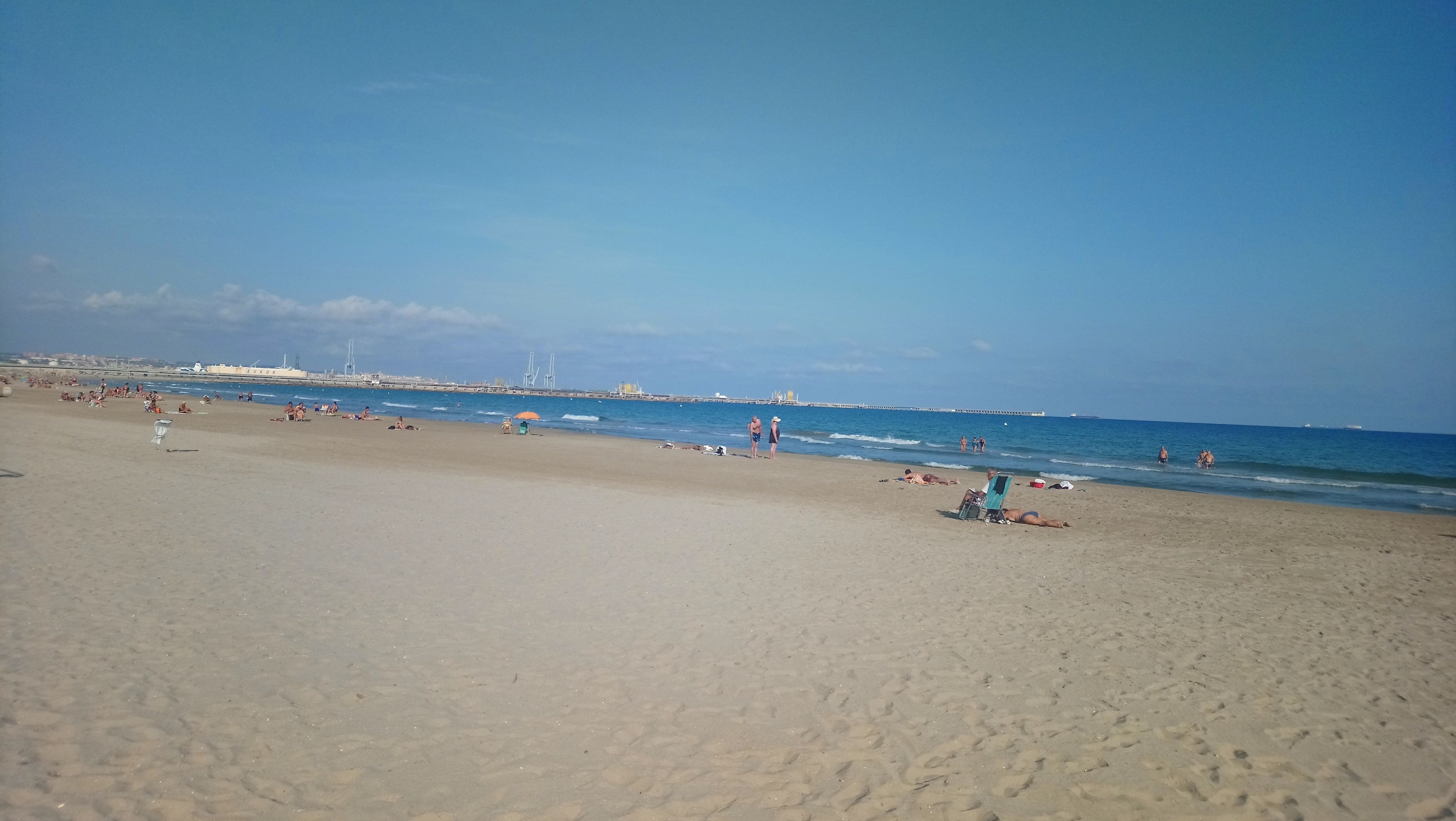 Een breed zandstrand met mensen die zonnebaden en zwemmen.