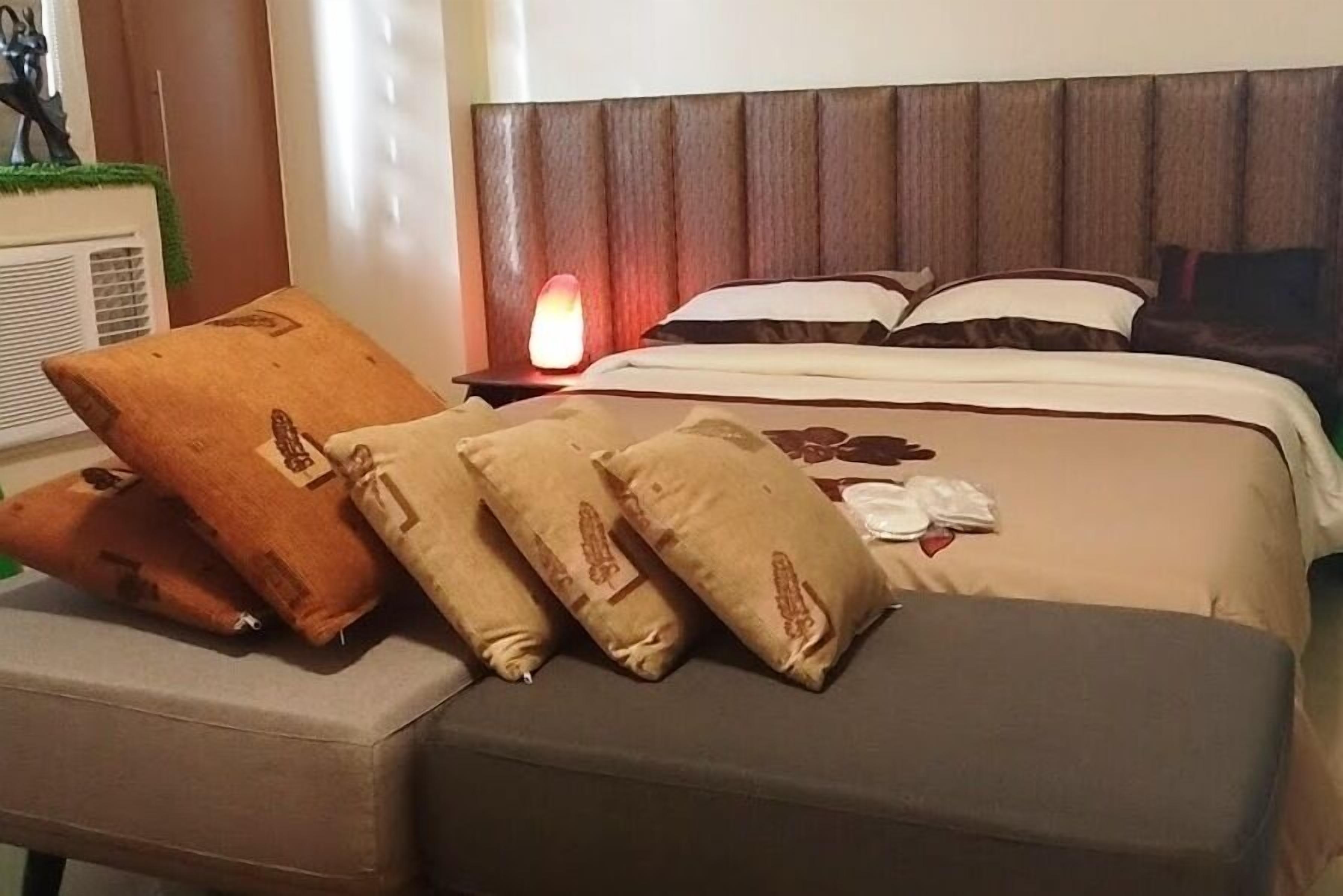 A hotel room with a bed, pillows, a bedside table with a lamp, and a small table with a decorative item.