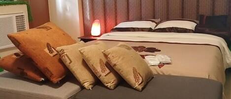 A hotel room with a bed, pillows, a bedside table with a lamp, and a small table with a decorative item.