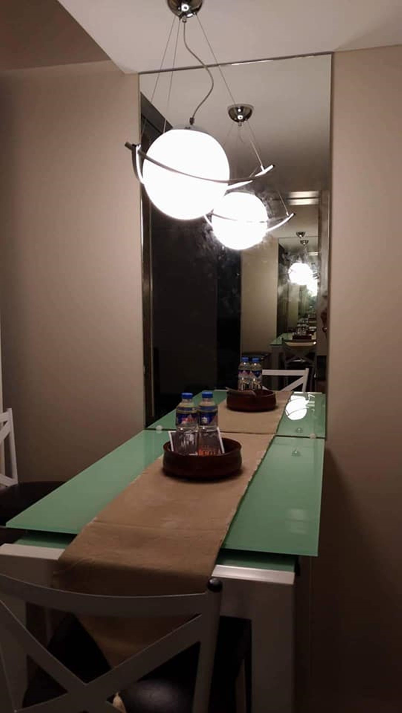 Ett rum med ett långt bord, en stol, en spegel och en taklampa.