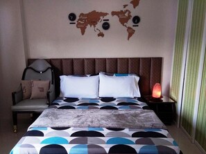 Habitación de hotel con cama, una silla, mesita de noche con lámpara y un mapa mundial en la pared.