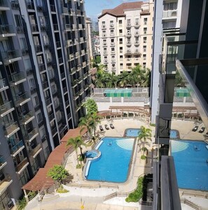 Un edificio de gran altura con múltiples balcones, un área de piscina con dos piscinas y una zona de estar cubierta.