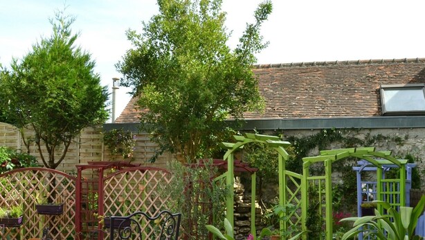 Eine Terrasse mit Tisch und Stühlen, umgeben von Grünpflanzen und einem Holzzaun.
