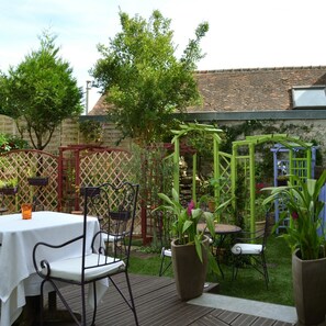 Eine Terrasse mit Tisch und Stühlen, umgeben von Grünpflanzen und einem Holzzaun.