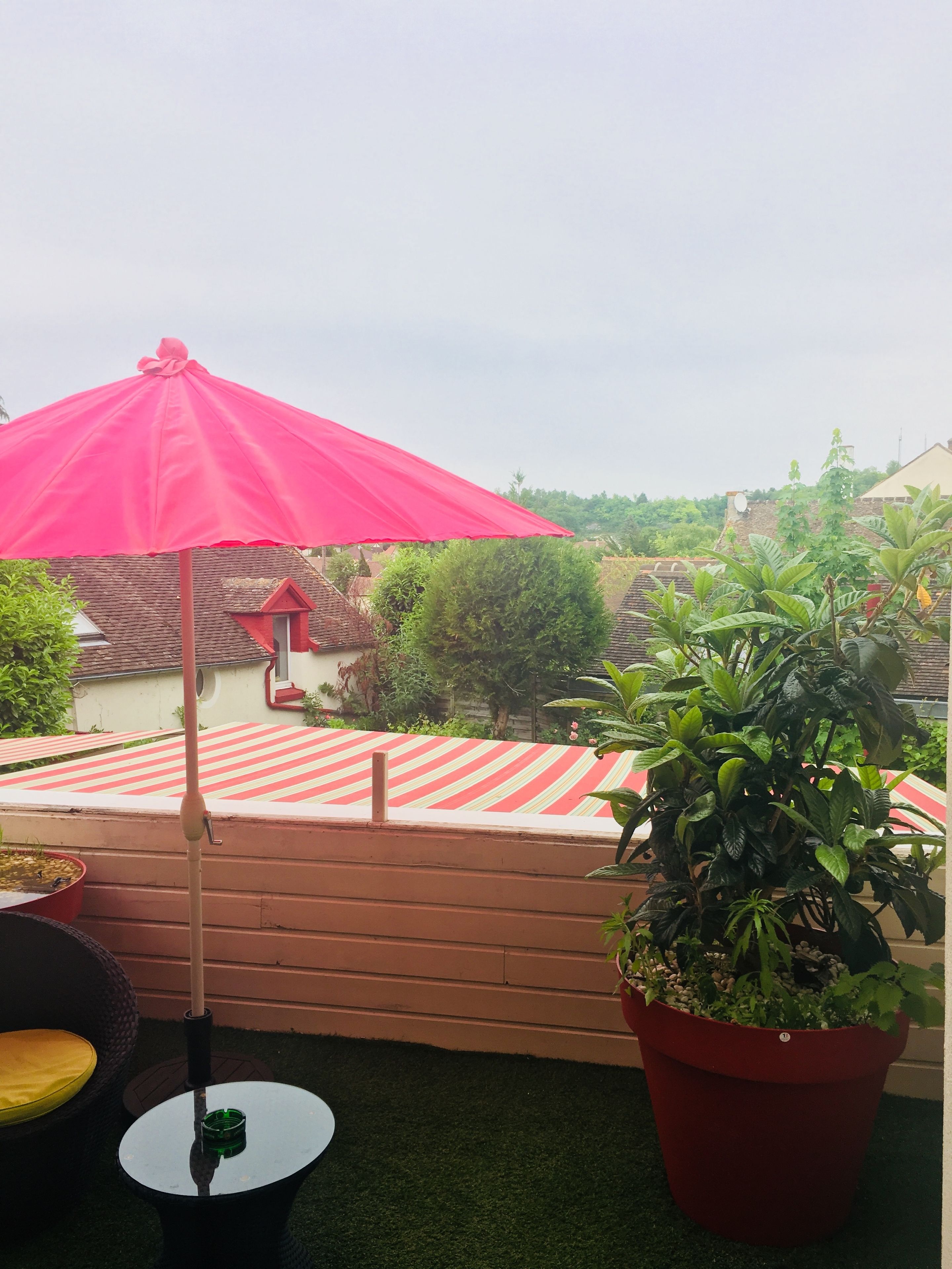 Un patio con un paraguas rojo, un mantel a rayas y plantas en macetas.