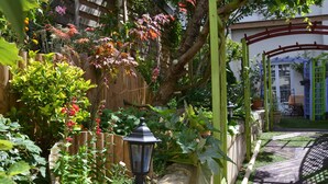 Ein Garten mit Holzzaun, Steinmauer und einer Pergola mit Kletterpflanzen.