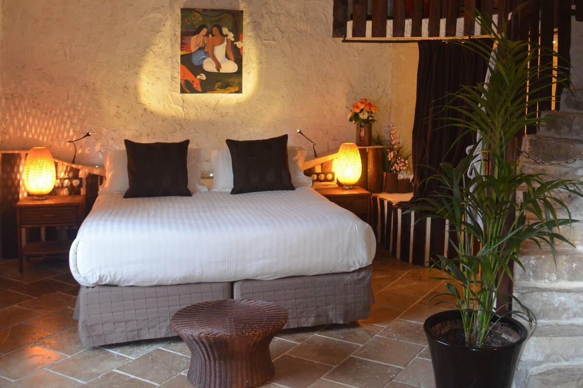 Une chambre à coucher avec un lit, des lampes de chevet, un tableau, un escalier et une plante en pot.