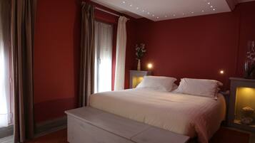 A bedroom with a large bed, a bench, a nightstand with a lamp, and a vase with flowers.
