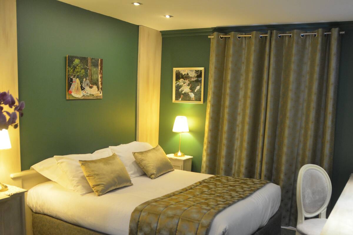 Une chambre d’hôtel avec un lit, un bureau, une chaise, une lampe et deux tableaux au mur.