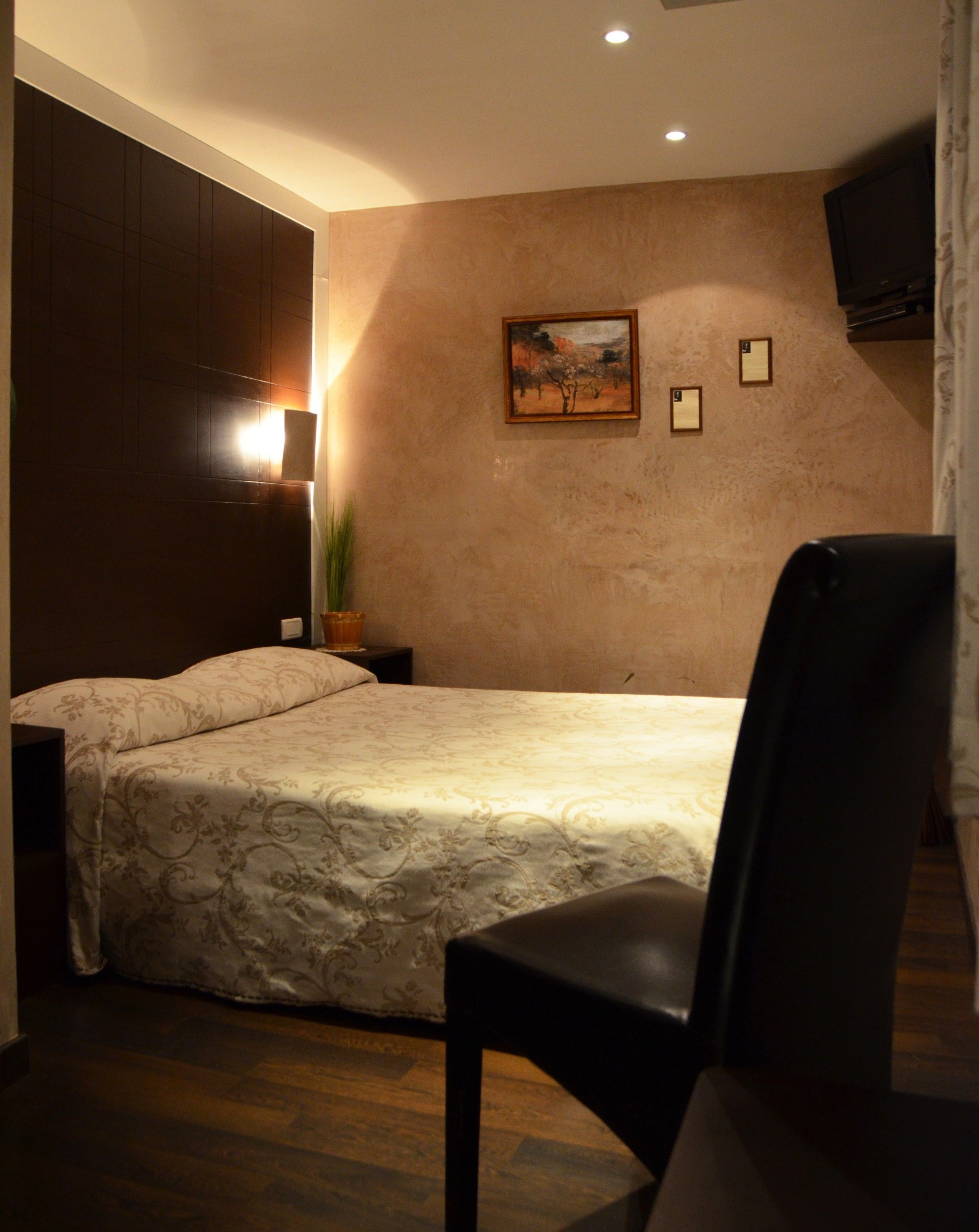 Une chambre à coucher comprenant un lit, une chaise, une table de chevet, une lampe, un tableau et un téléviseur.