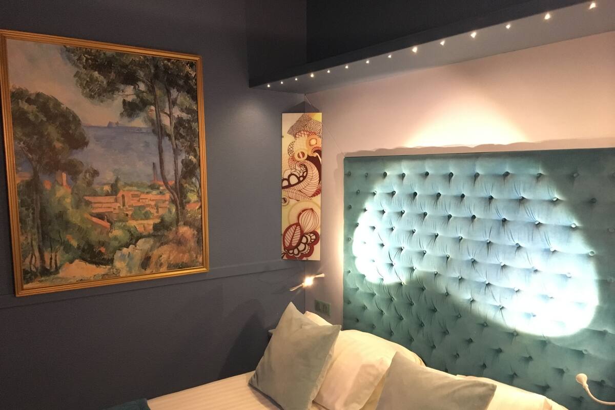 Une chambre à coucher avec une tête de lit capitonnée, un tableau représentant un paysage et un panneau décoratif.