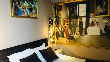 A hotel room with a large bed, a nightstand, a lamp, and two paintings on the wall.