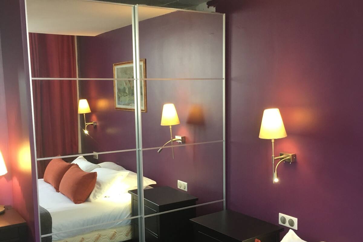 Une chambre d’hôtel équipée d’un lit, d’un bureau, d’un miroir et de deux lampes fixées au mur.