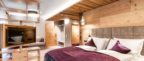 A modern bedroom with a wooden ceiling, a large bed with white and purple bedding, a TV on a wooden stand, and a built-in wardrobe.