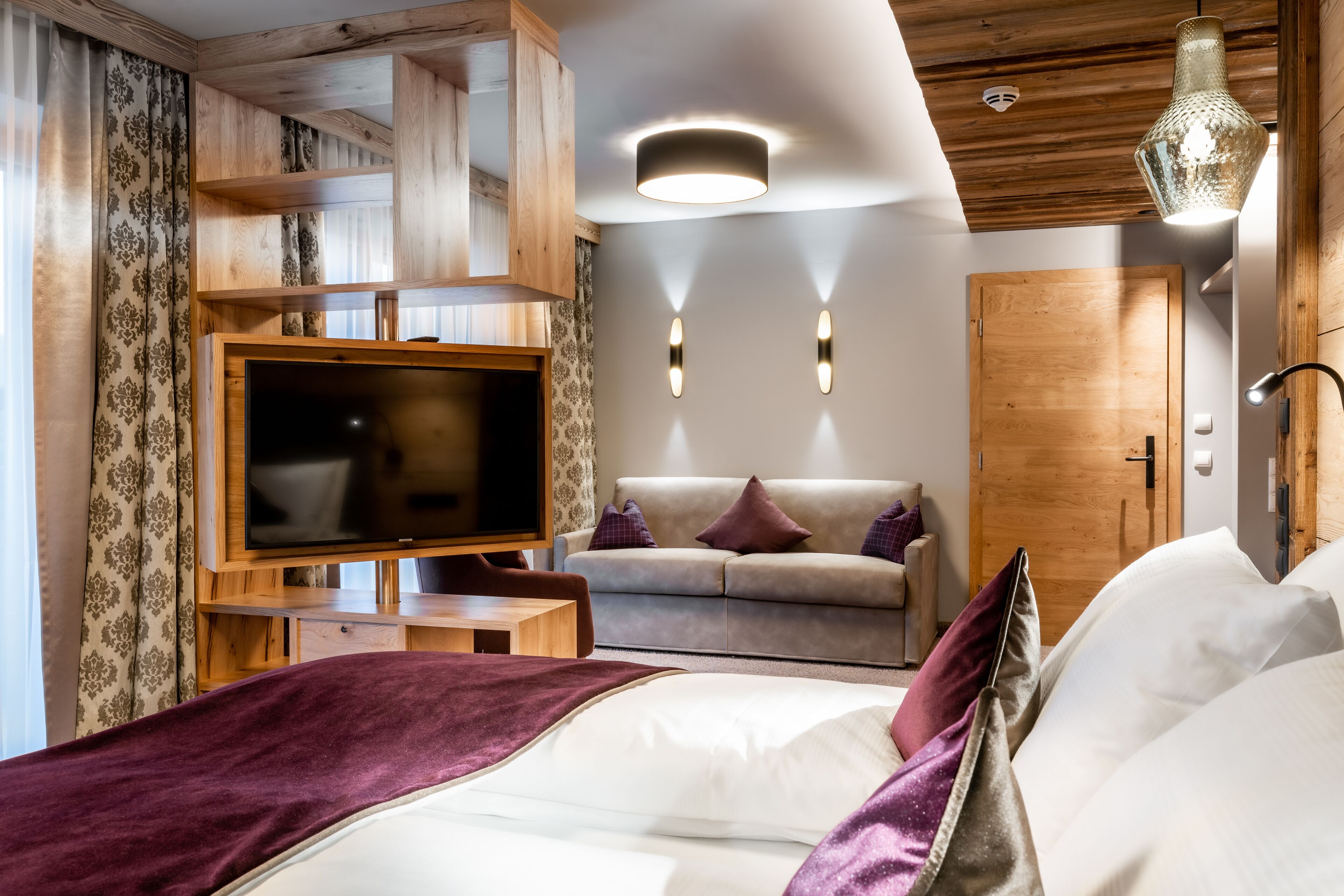 Una habitación de hotel moderna con una cama grande, un televisor, un sofá y techo de madera.