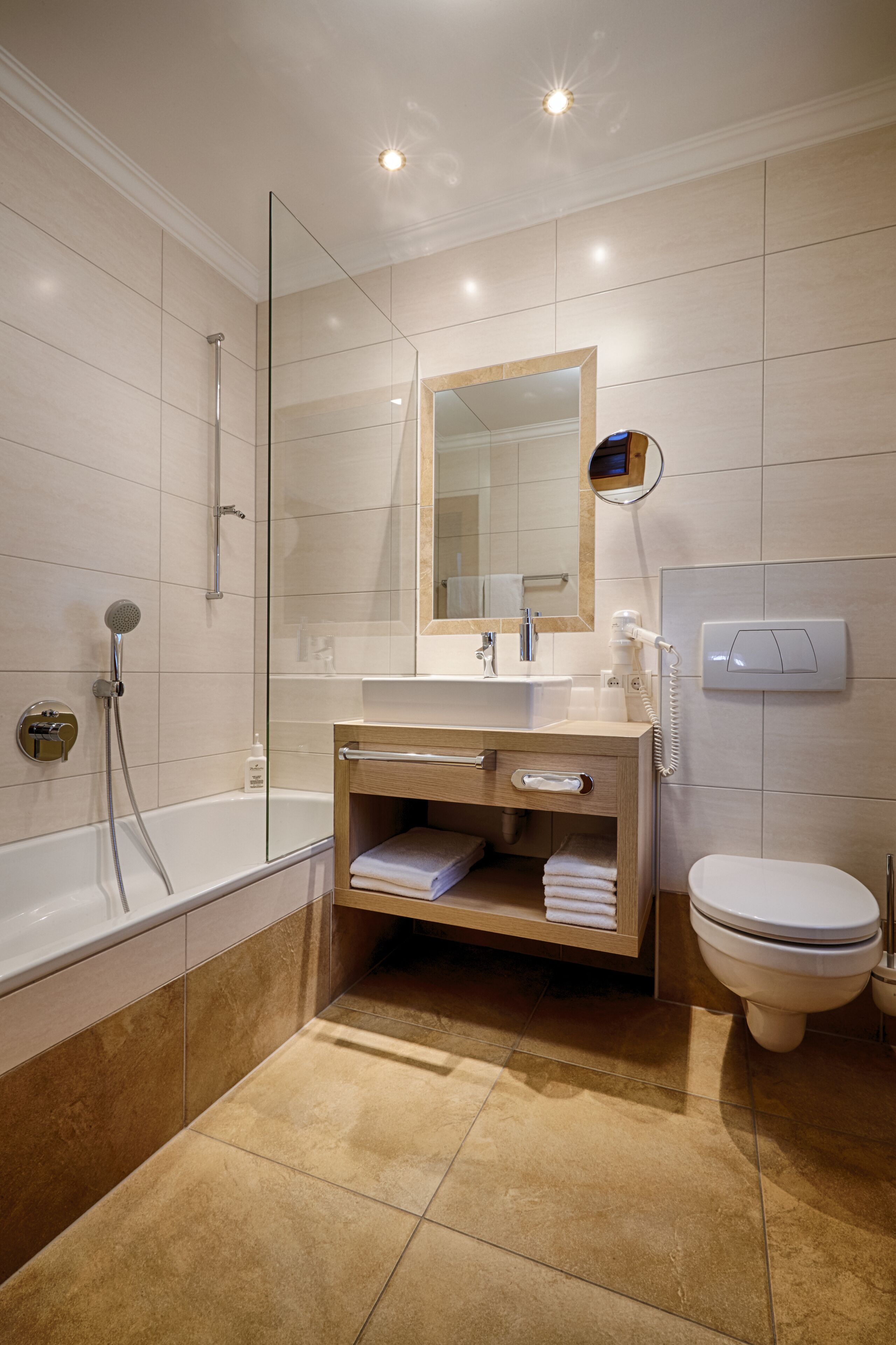 Un bagno moderno con doccia vetrata, mobile lavabo in legno con specchio, water e porta asciugamani a incasso.