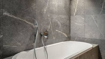 A modern bathroom with a freestanding bathtub, marble walls, and a showerhead.