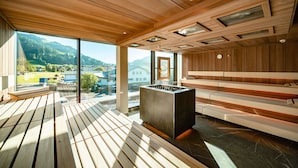 Sala de sauna com bancos de madeira, aquecedor central e amplas janelas com vista para o exterior.