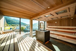 Una sauna con panche in legno, una stufa centrale e ampie finestre con vista sull'esterno.
