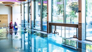 Piscina interior moderna com paredes de vidro e luminárias circulares.