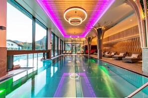 Una piscina interior moderna con vistas a montañas, amplios ventanales y un área de descanso con asientos.