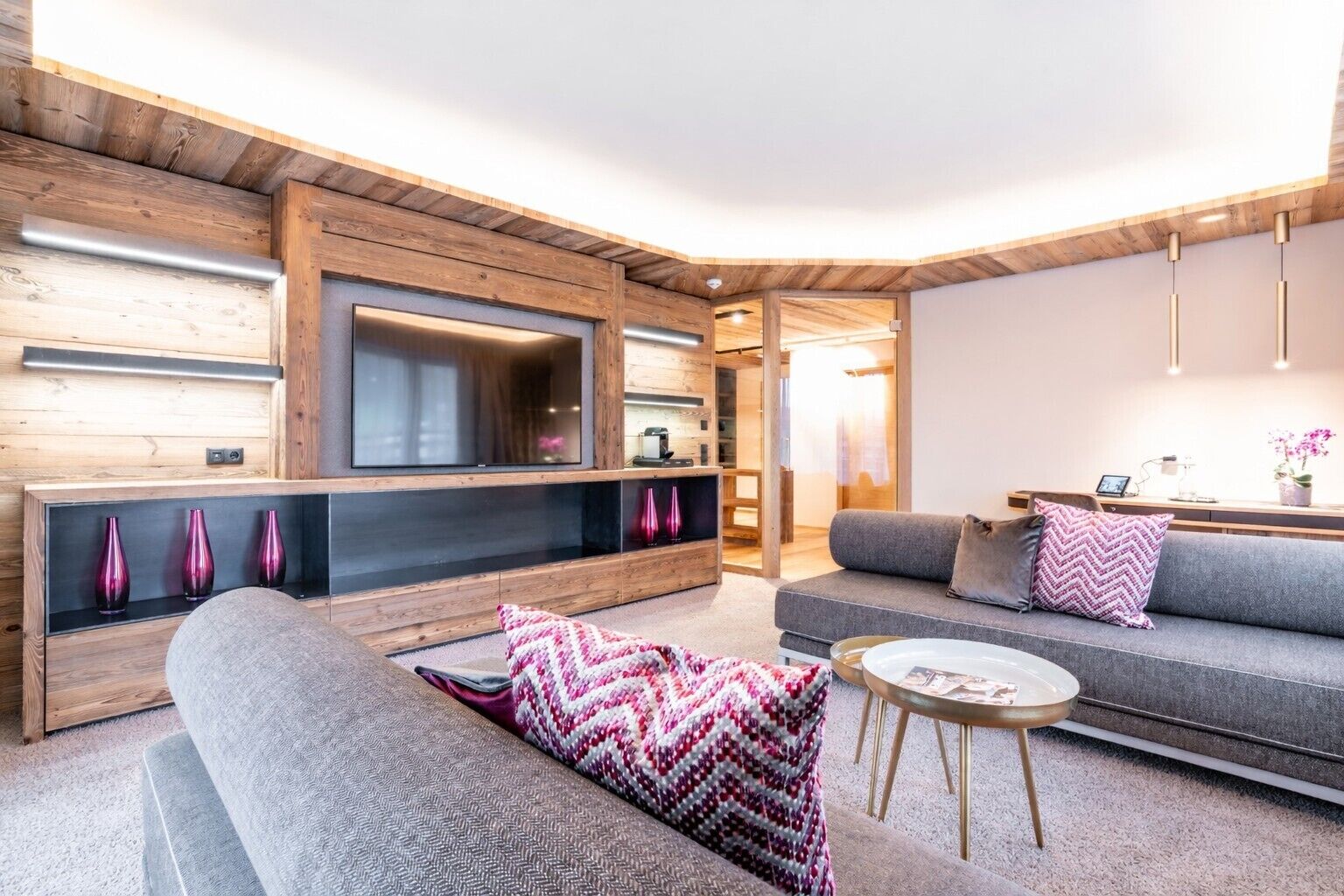 Una sala de estar moderna con televisor de pantalla plana, sofás grises, una mesa de centro y detalles de madera.