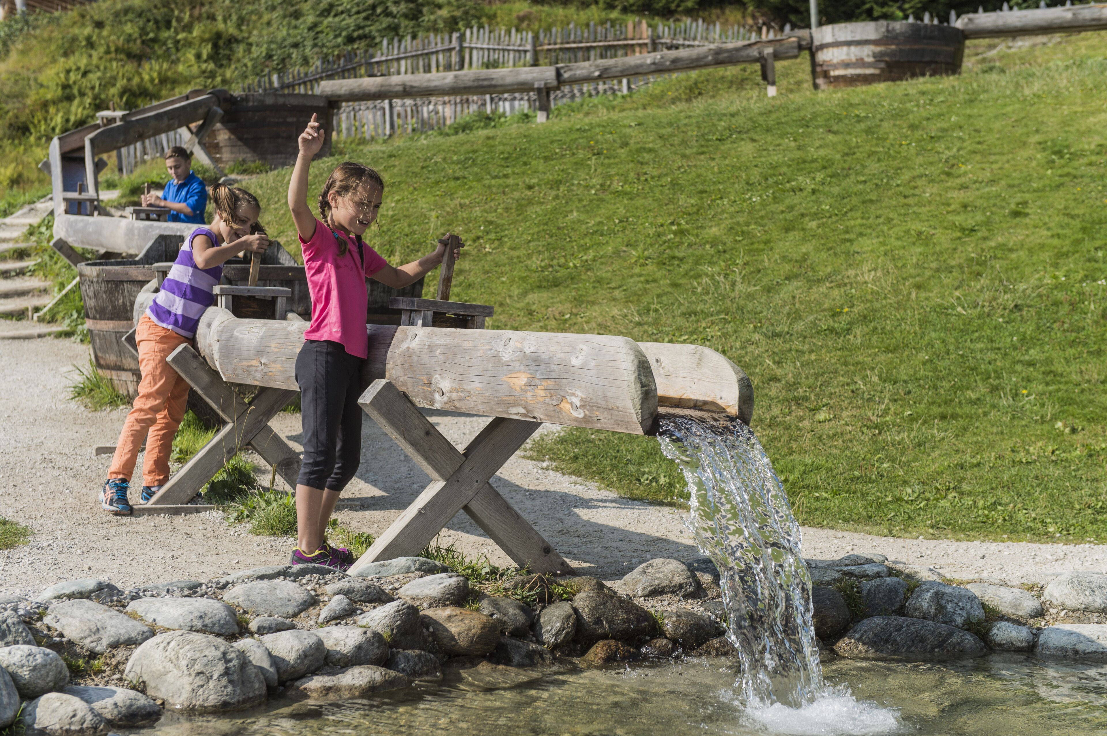 A wooden water feature with a young girl and another child interacting with it.