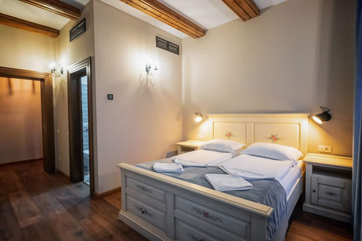 Quarto com cama, mesas de cabeceira e apoio para objetos.