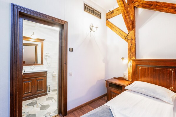 Un dormitorio con cabecera de madera, una cama con ropa de cama blanca, una mesita de noche y un aparador de madera con espejo.