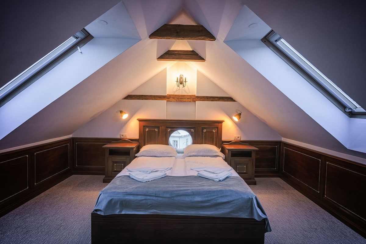 Quarto com teto abobadado, cama com almofadas, mesas de cabeceira e uma janela circular acima da cama.