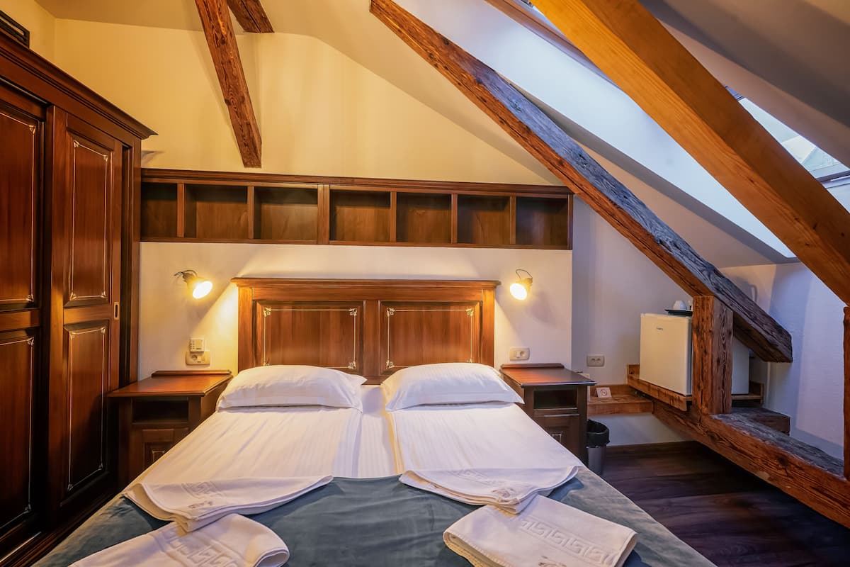 Quarto com duas camas, vigas de madeira, um claraboia e um frigorífico pequeno.