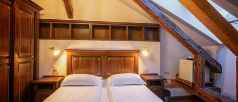 A bedroom with two beds, wooden beams, a skylight, and a small refrigerator.