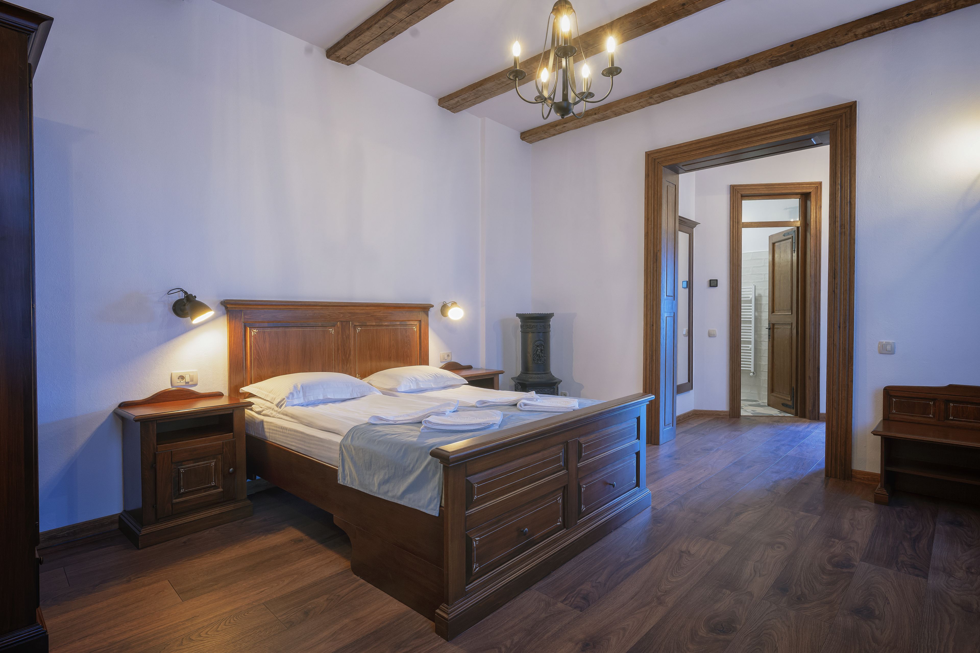 A bedroom with a wooden bed, nightstands, a chandelier, and a hallway leading to another room.