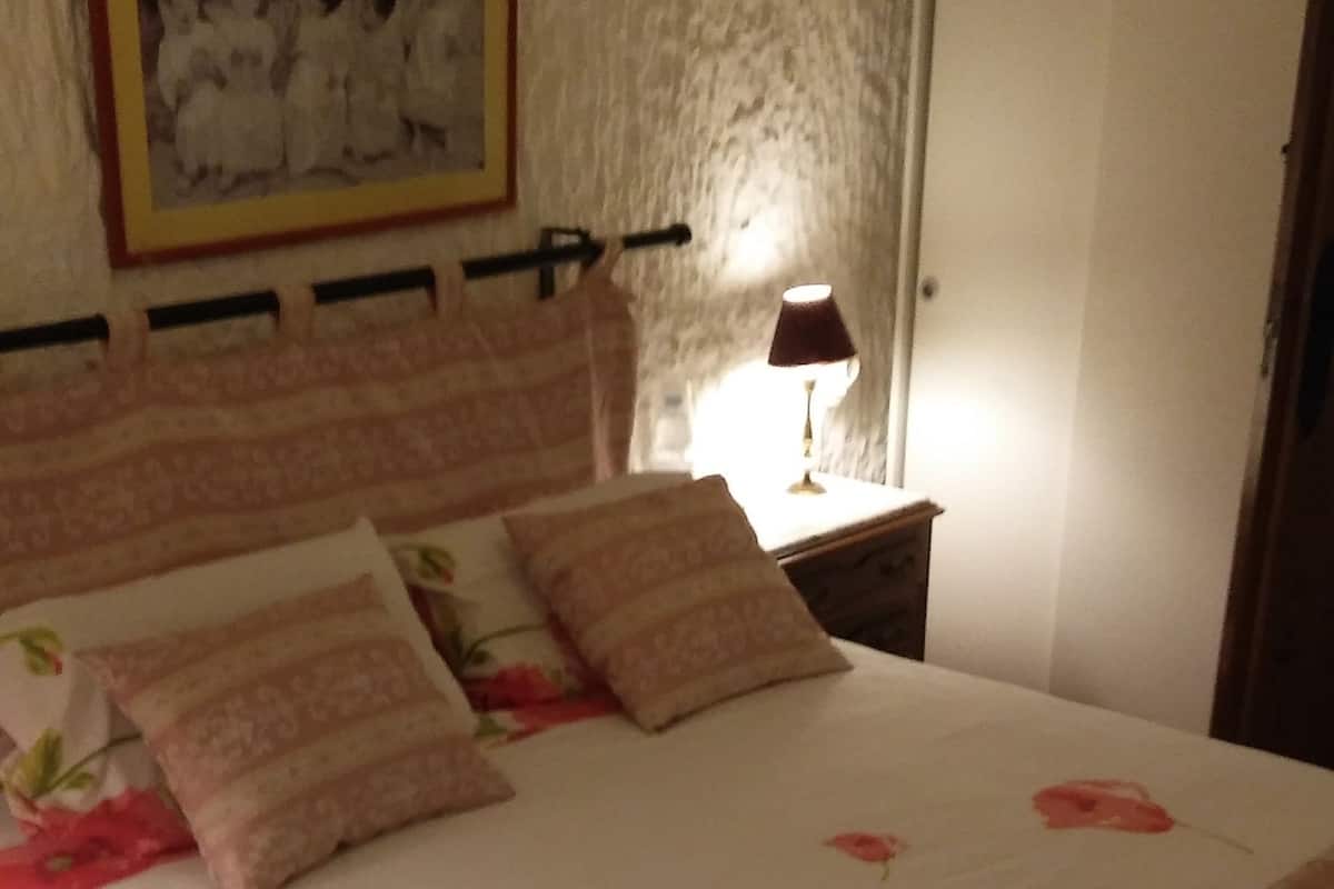Une chambre à coucher avec un lit, des oreillers, une table de chevet, une lampe et une porte.