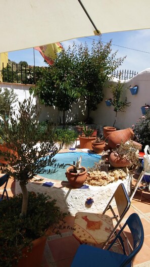 A sunny outdoor area with a pool, potted plants, and a chair. - Cuevaalegria (Guadix)
