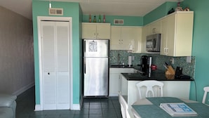 A compact kitchen with a refrigerator, microwave, and a small dining area with a table and chairs. - Stunning ocean front condo with an extraordinary view of the Fabulous Boardwalk! (Carolina Beach)