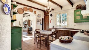 A rustic kitchen with wooden beams, a dining area with a table and chairs, and a green cabinet. - House / Villa - Marina di Ragusa, Ragusa (Marina di Ragusa)