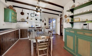 A kitchen with a tiled floor, wooden cabinets, a dining table with chairs, and various kitchen utensils and appliances.