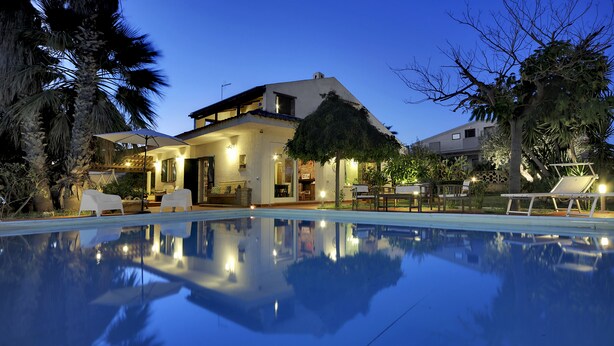 A house with a swimming pool, patio furniture, and a well-lit interior. - House / Villa - Marina di Ragusa, Ragusa (Marina di Ragusa)
