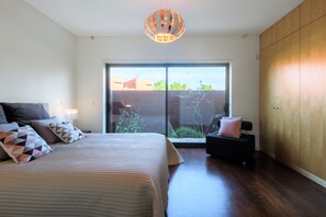 A bedroom with a large bed, a nightstand, a black bench, and a sliding glass door leading to a balcony. - L'Orangerie (Vilamoura)