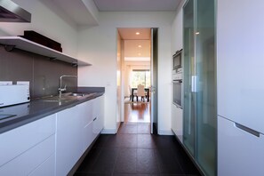 A modern kitchen with white cabinetry, a dark tiled floor, and a glass-front refrigerator. - L'Orangerie (Vilamoura)