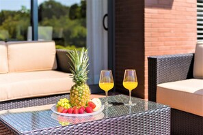 A glass-top table with a fruit platter, two glasses of orange juice, and wicker furniture on a balcony. - L'Orangerie (Vilamoura)