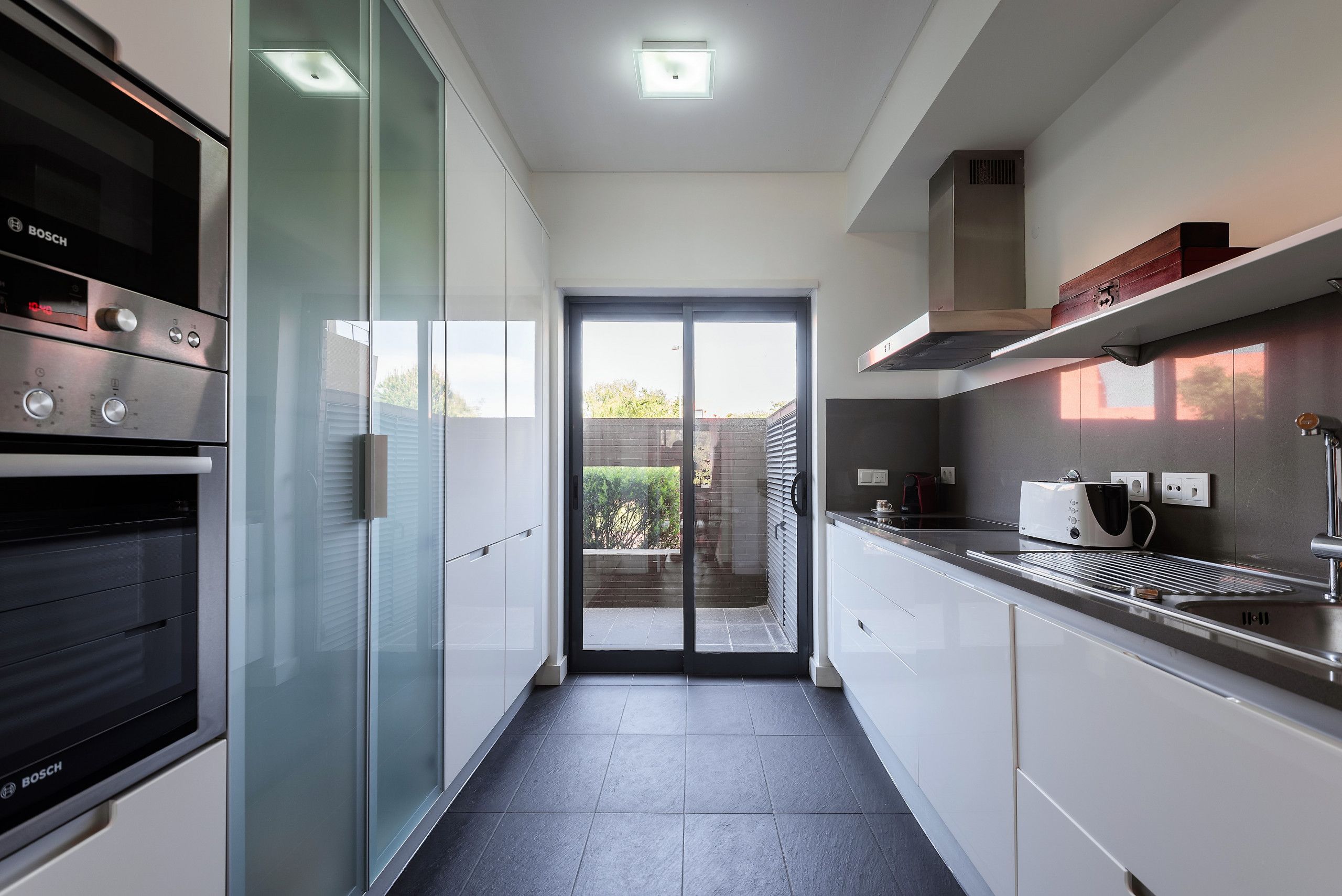 Eine moderne Küche mit Backofen von Bosch, einer Glastürspeisekammer und Blick ins Freie.